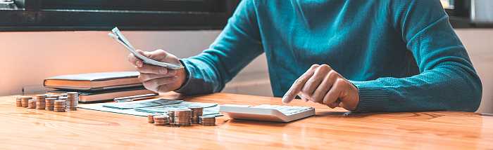 Man pressing calculator buttons to figure budget.